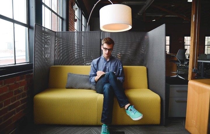 Man sitting on a yellow sofa under a bent over large floor lamp